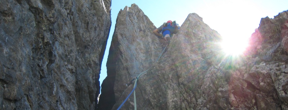 A climber ascending a sunlit rock chimney on a rope.
